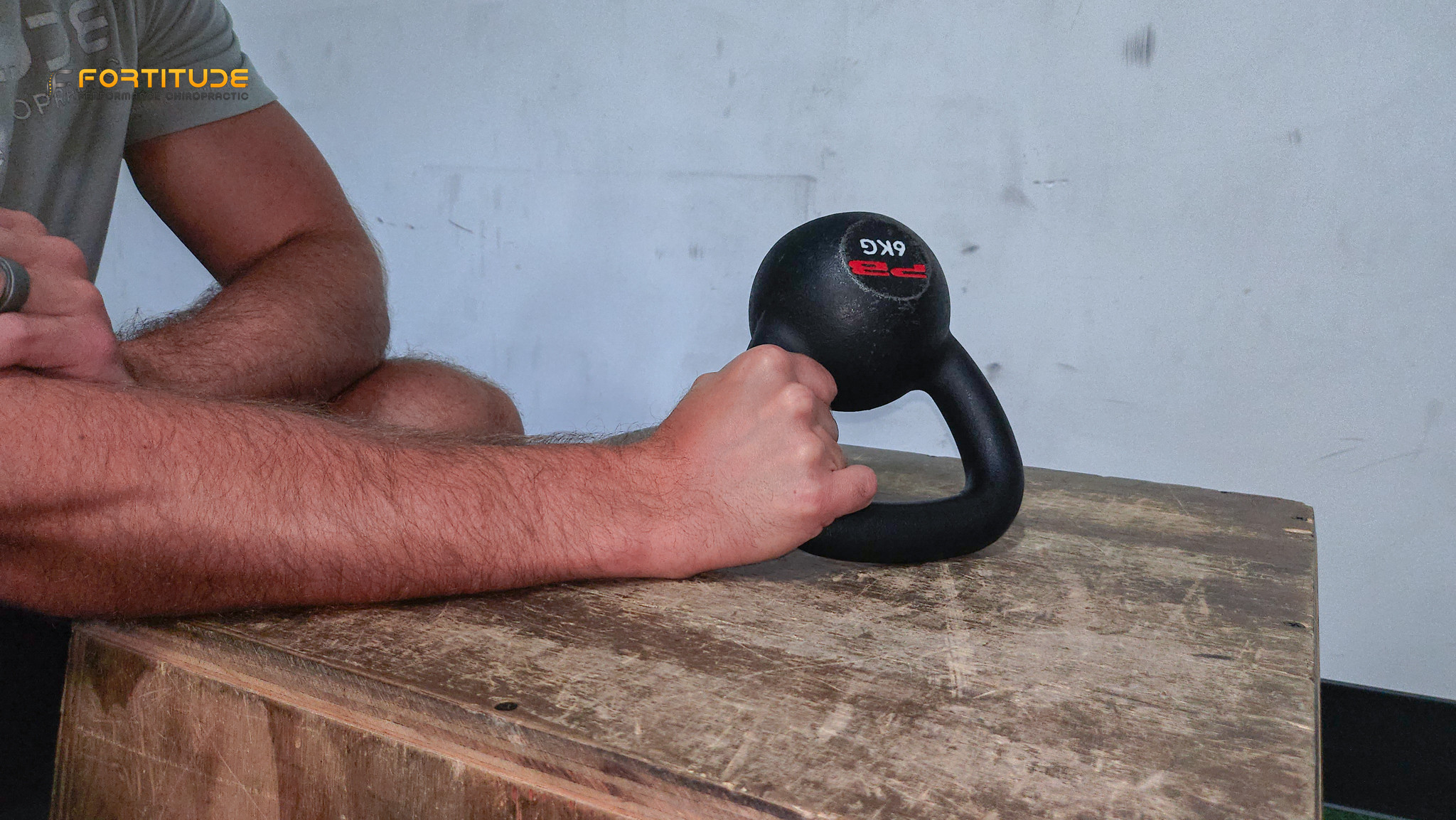 forearm supported kettlebell hold for wrist strength and grip rehab, shown on wooden box in training facility