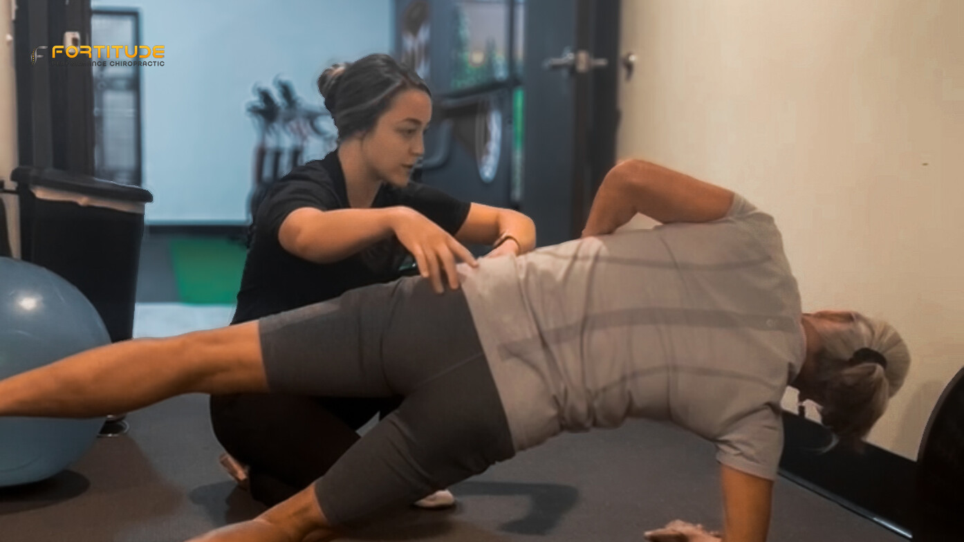 Chiropractor guiding a core stability drill with a water bottle on the back to train spinal control in golfers.