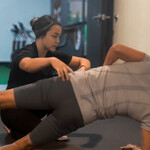 Chiropractor guiding a core stability drill with a water bottle on the back to train spinal control in golfers.