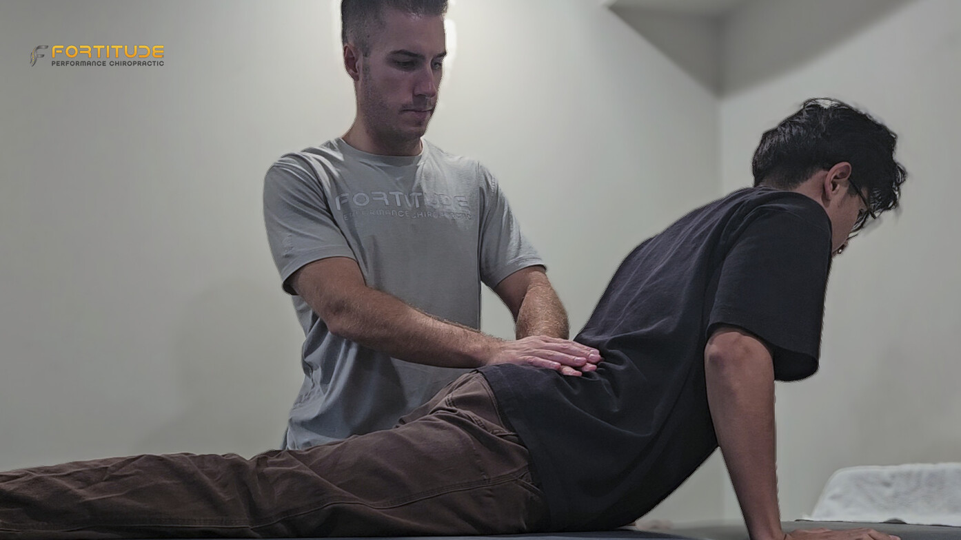 Chiropractor guiding patient through prone press-up exercise to relieve lower back tension and sciatic nerve pressure.