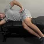 Patient performing side-lying leg hang on chiropractic table to decompress lumbar spine and reduce sciatic nerve irritation.