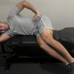 Patient performing side-lying leg hang on chiropractic table to decompress lumbar spine and reduce sciatic nerve irritation.