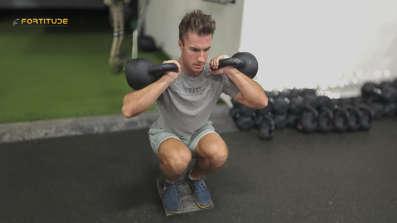 Male athlete performing a front-loaded squat on slant boards